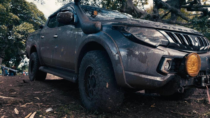Mud-splattered black Pick-up truck parked on a dirt ground with trees and fallen leaves in the background. Mud-splattered black Pick-up truck parked on a dirt ground with trees and fallen leaves in the background.