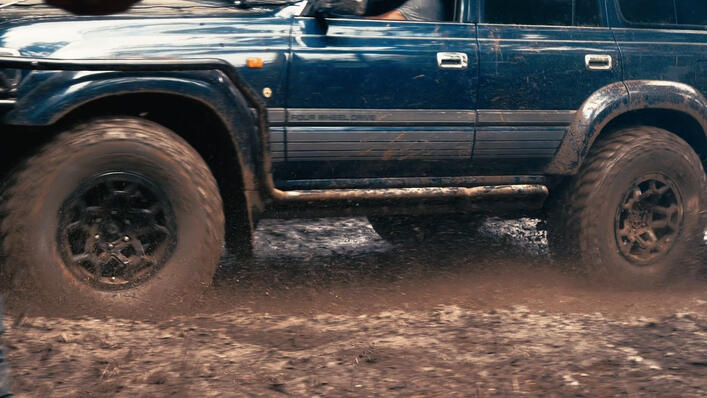Modified Toyota Land Cruiser driving through deep mud during an off-road 4x4 adventure, splashing water across a challenging muddy trail.